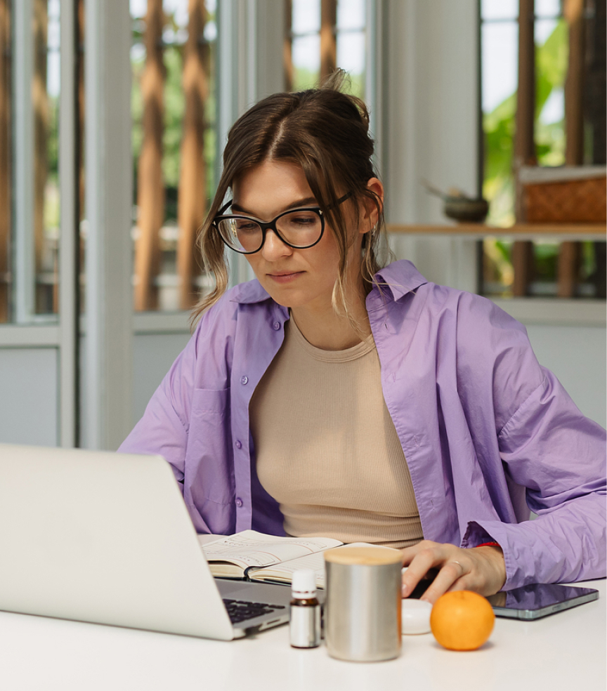 Kobieta w okularach siedzi przy stole i pracuje na laptopie